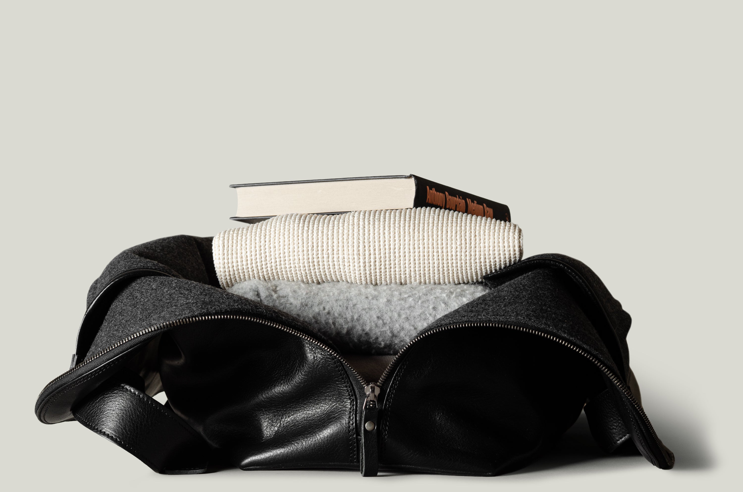 Black leather duffel bag with books inside on a light gray background