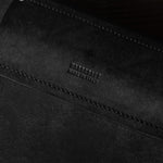 Close-up of a black leather bag with visible stitching and brand name on a dark background