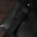 Close-up of a black bag with a belt and metal rivet on a wooden surface