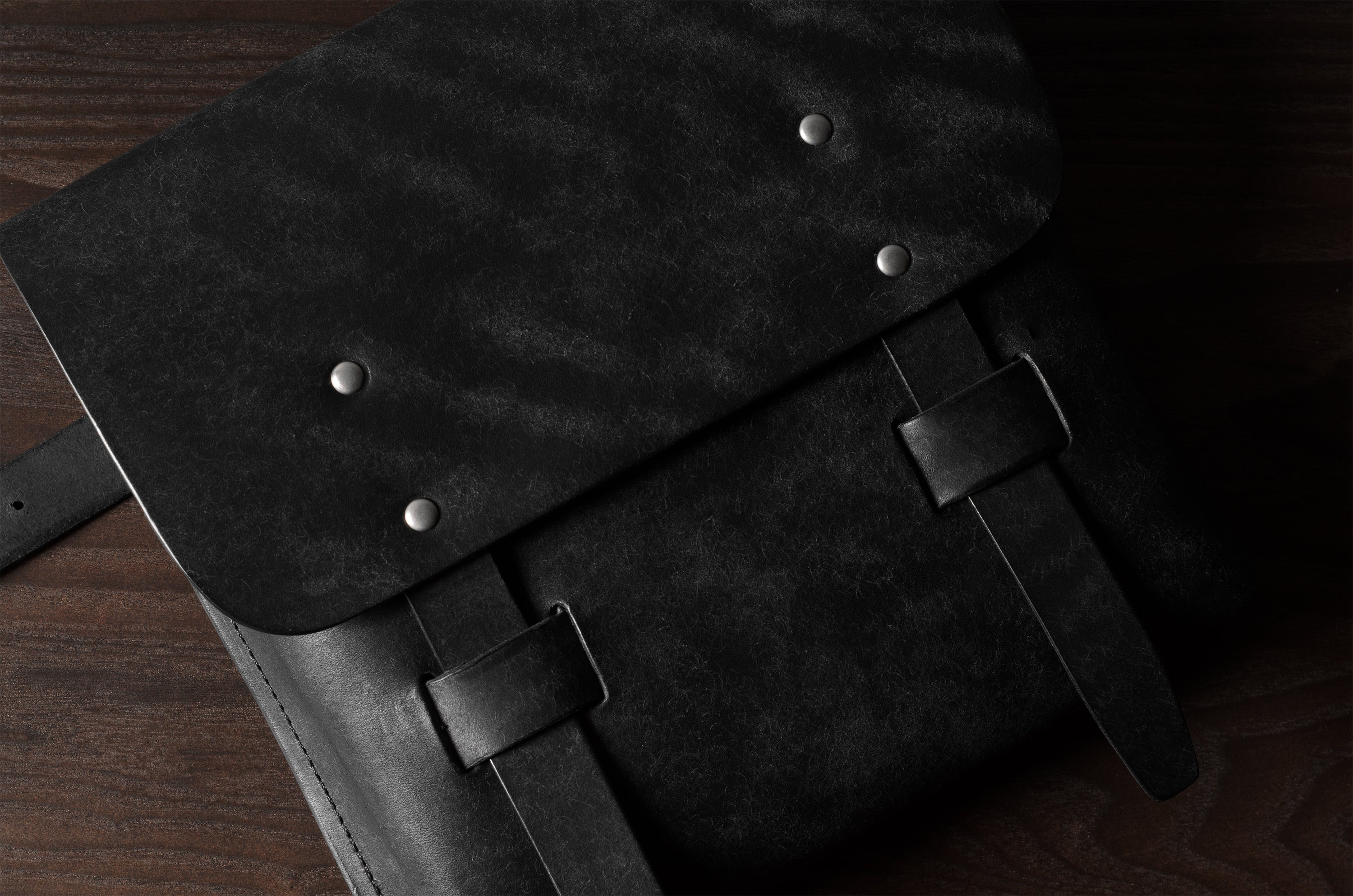Close-up of a black leather bag with metal rivets on a wooden surface