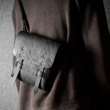 Person wearing a dark sweater with a gray leather satchel bag on a plain background