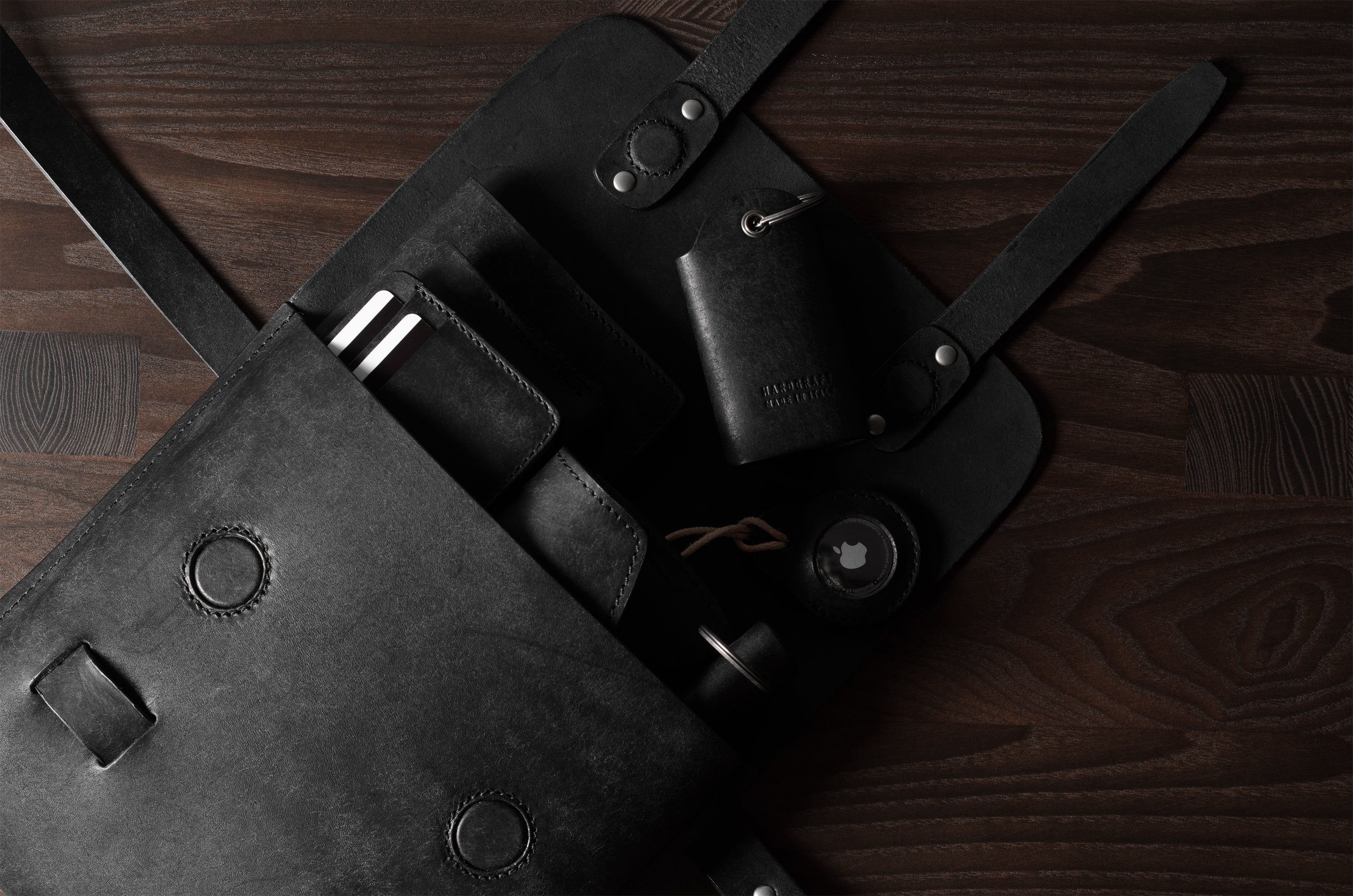 Black leather bag with multiple small leather goods on a wooden surface