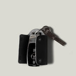 Black leather key holder with 2 metal buttons and car key fob inside on light grey background