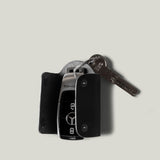 Black leather key holder with 2 metal buttons and car key fob inside on light grey background
