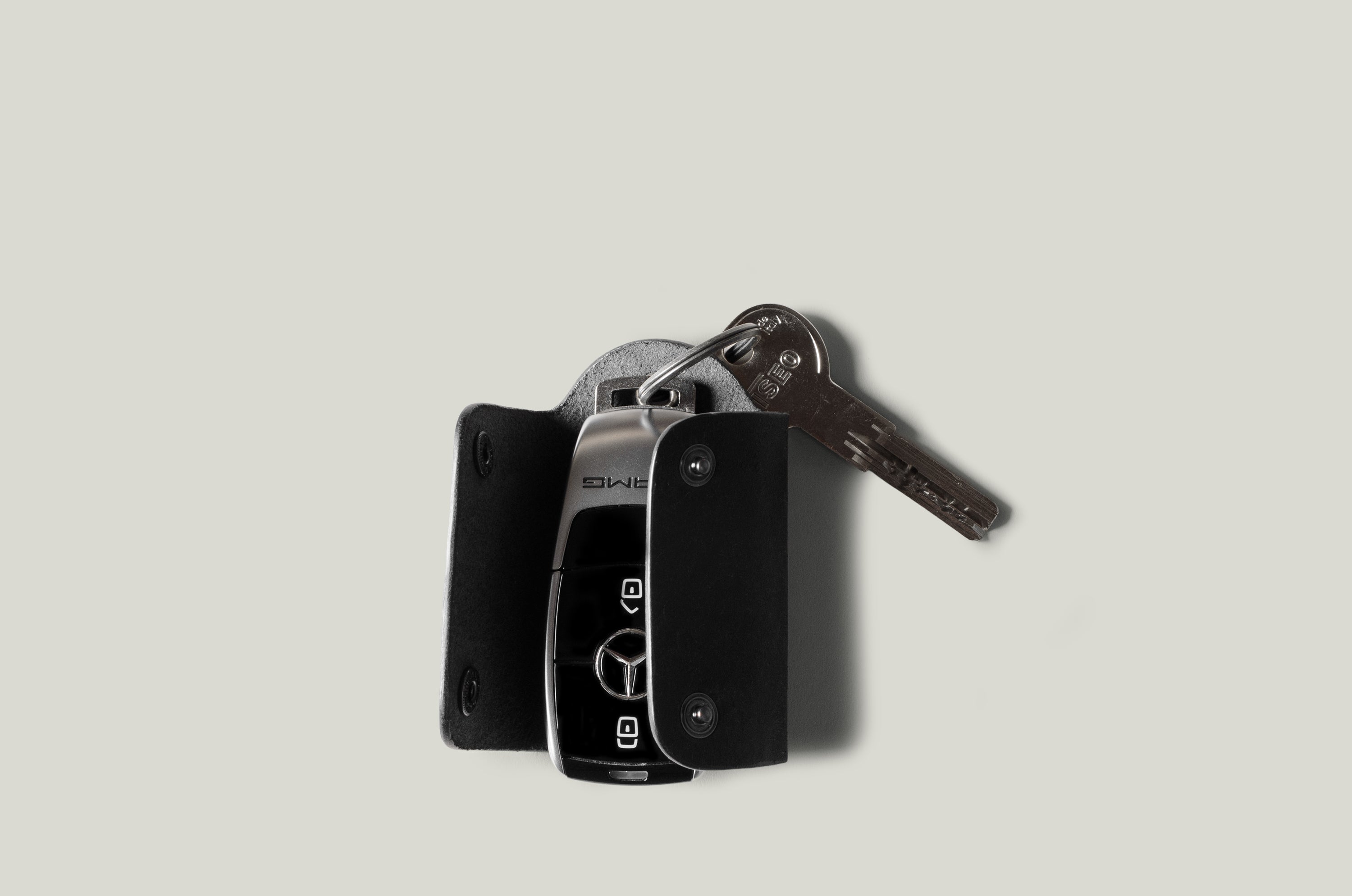 Black leather key holder with 2 metal buttons and car key fob inside on light grey background