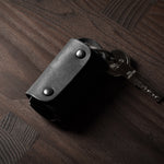 Black leather key holder with 2 metal buttons, showing keys on wood background