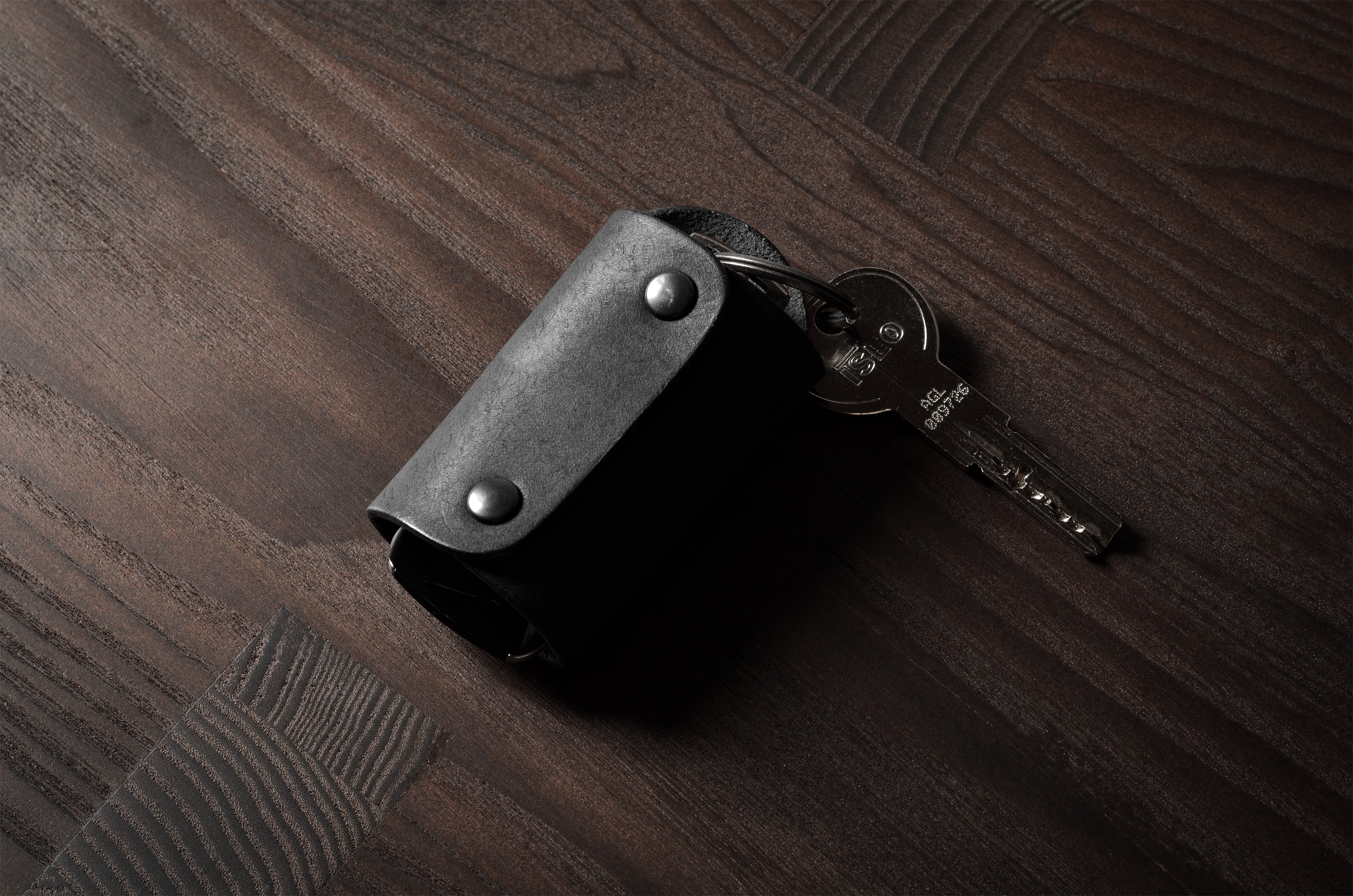 Black leather key holder with 2 metal buttons, showing keys on wood background