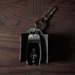 Black leather key holder with 2 metal buttons and car key fob inside on wood background
