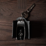 Black leather key holder with 2 metal buttons and car key fob inside on wood background