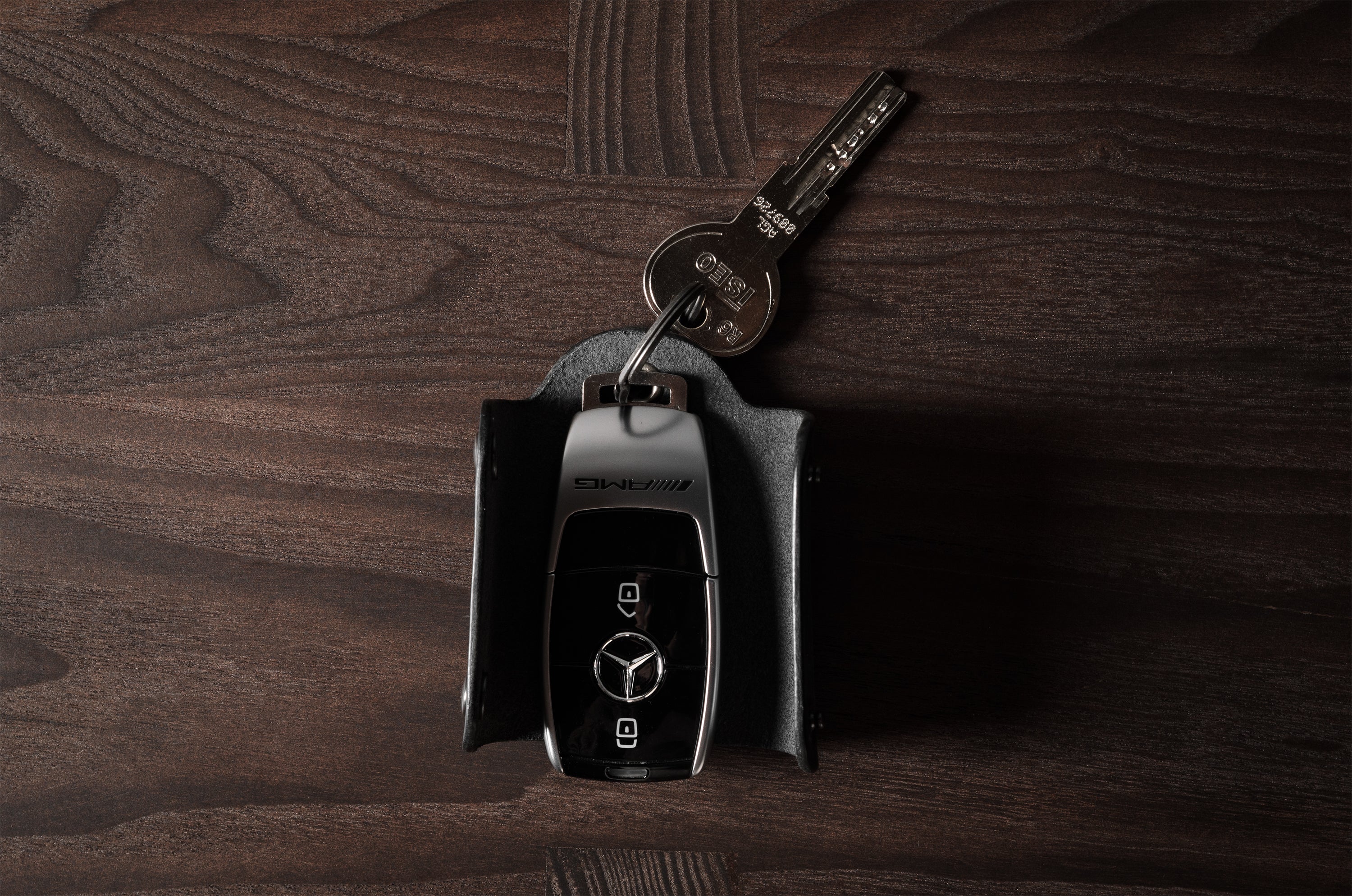 Black leather key holder with 2 metal buttons and car key fob inside on wood background
