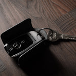 Black leather key holder with 2 metal buttons, showing keys and car key fob on wood background