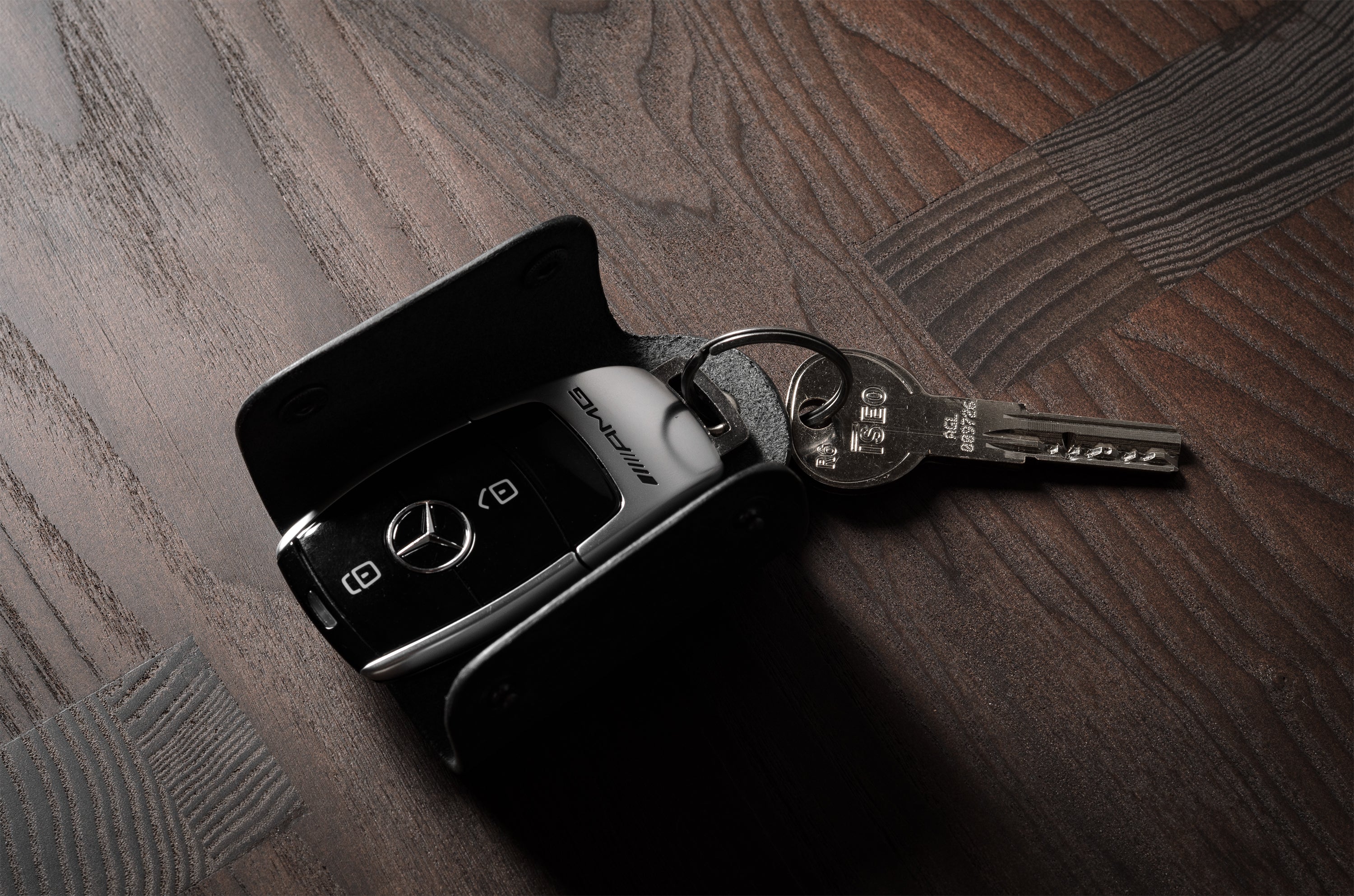Black leather key holder with 2 metal buttons, showing keys and car key fob on wood background