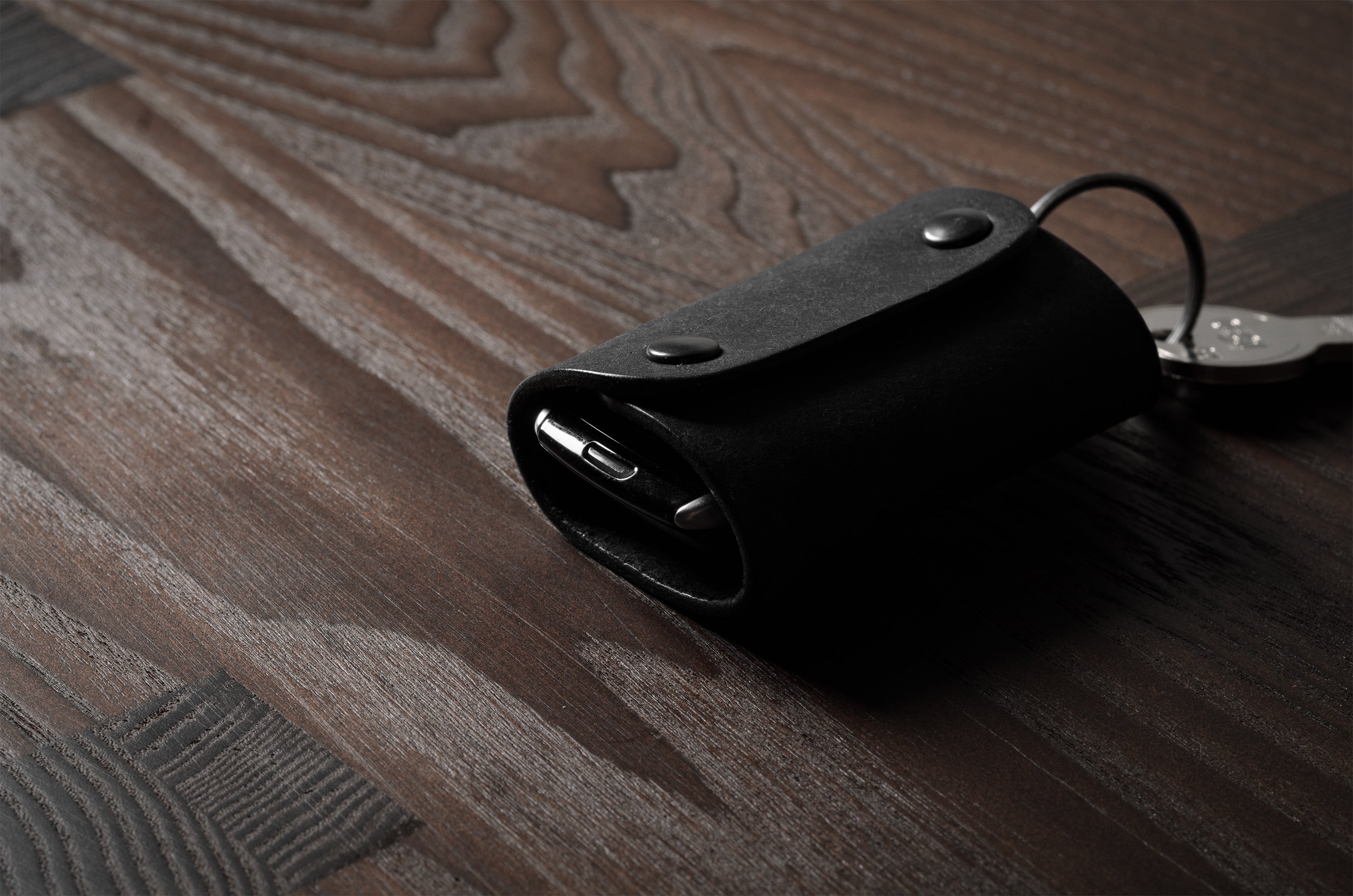 Black leather key holder with 2 metal buttons  on wood background