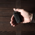 Black leather key holder with 2 metal buttons, held in hand on wood background