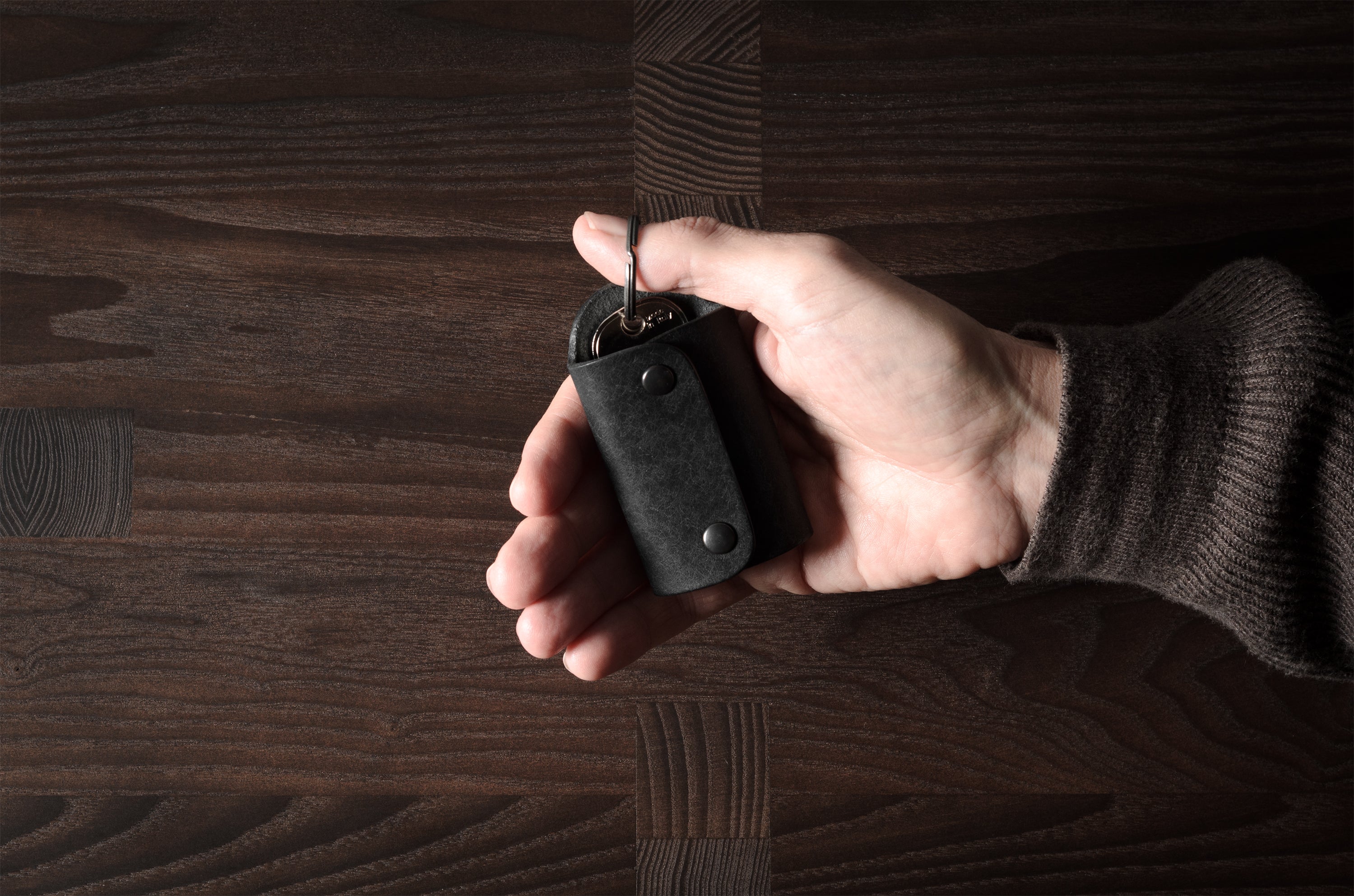Black leather key holder with 2 metal buttons, held in hand on wood background