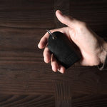 Black leather key holder with 2 metal buttons, held in hand on wood background