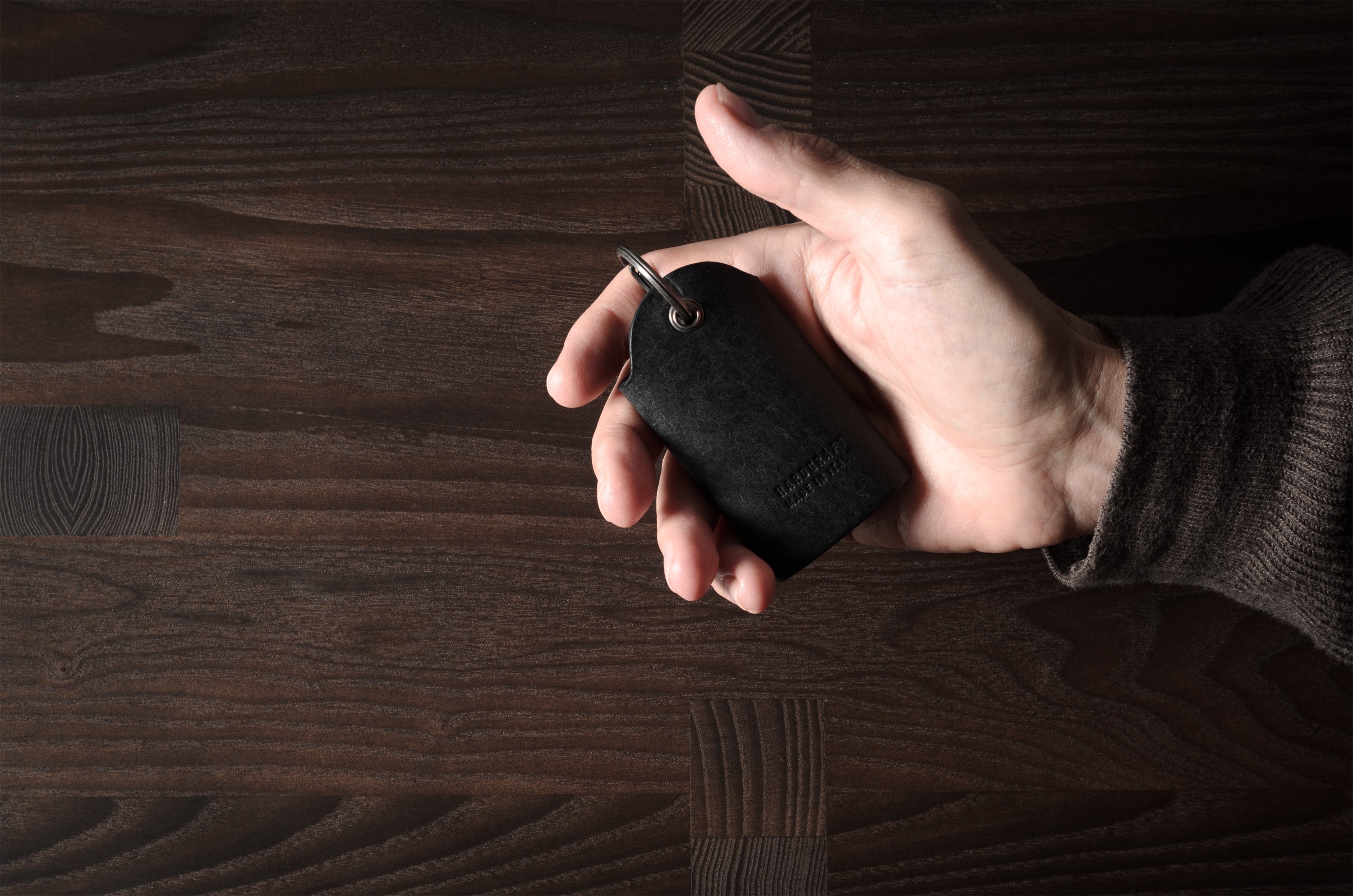 Black leather key holder with 2 metal buttons, held in hand on wood background