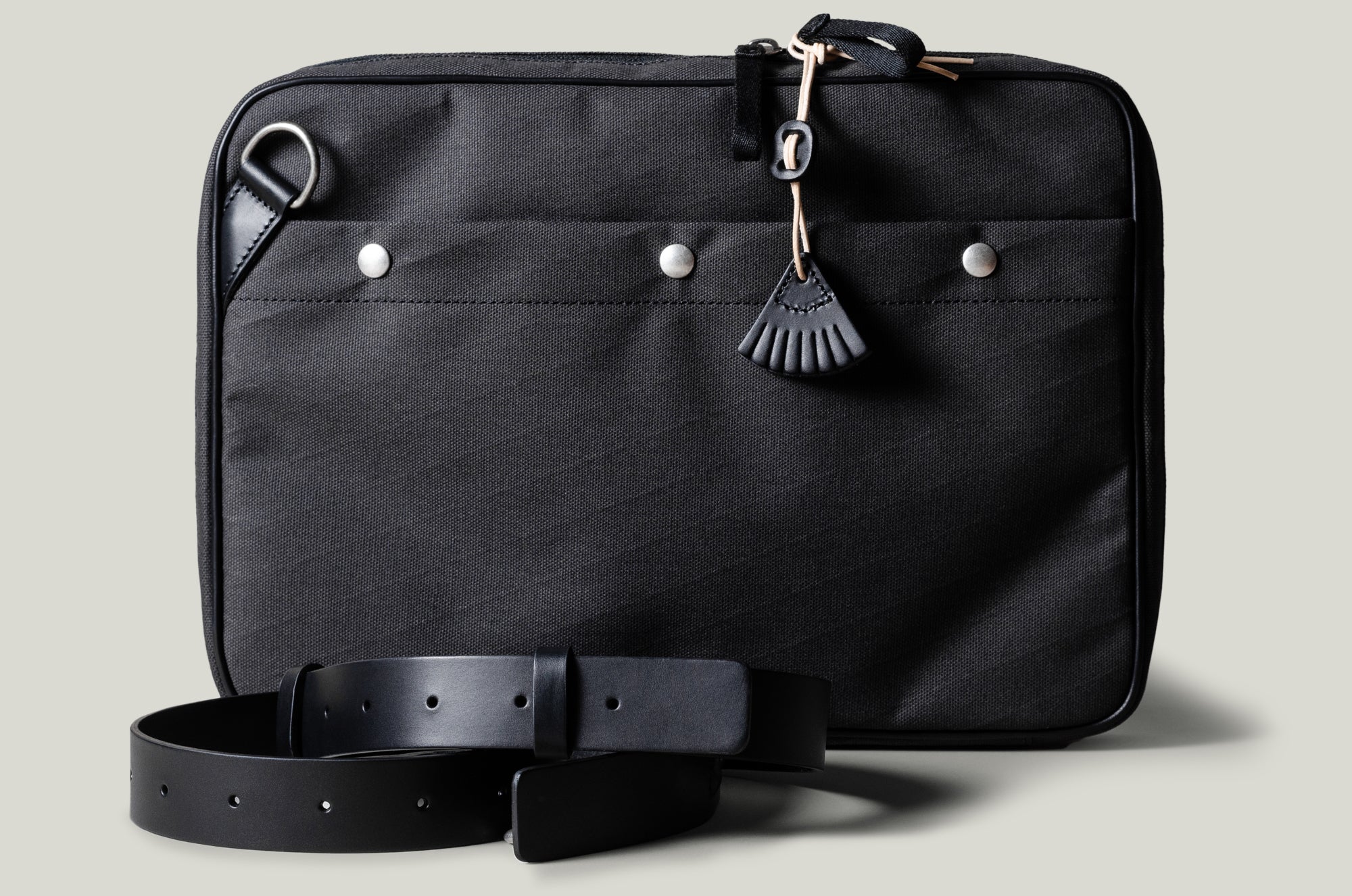 A charcoal-colored laptop bag with black leather straps and a brown wool-blend lining. It features a main compartment closed with a zipper and an additional exterior pocket.