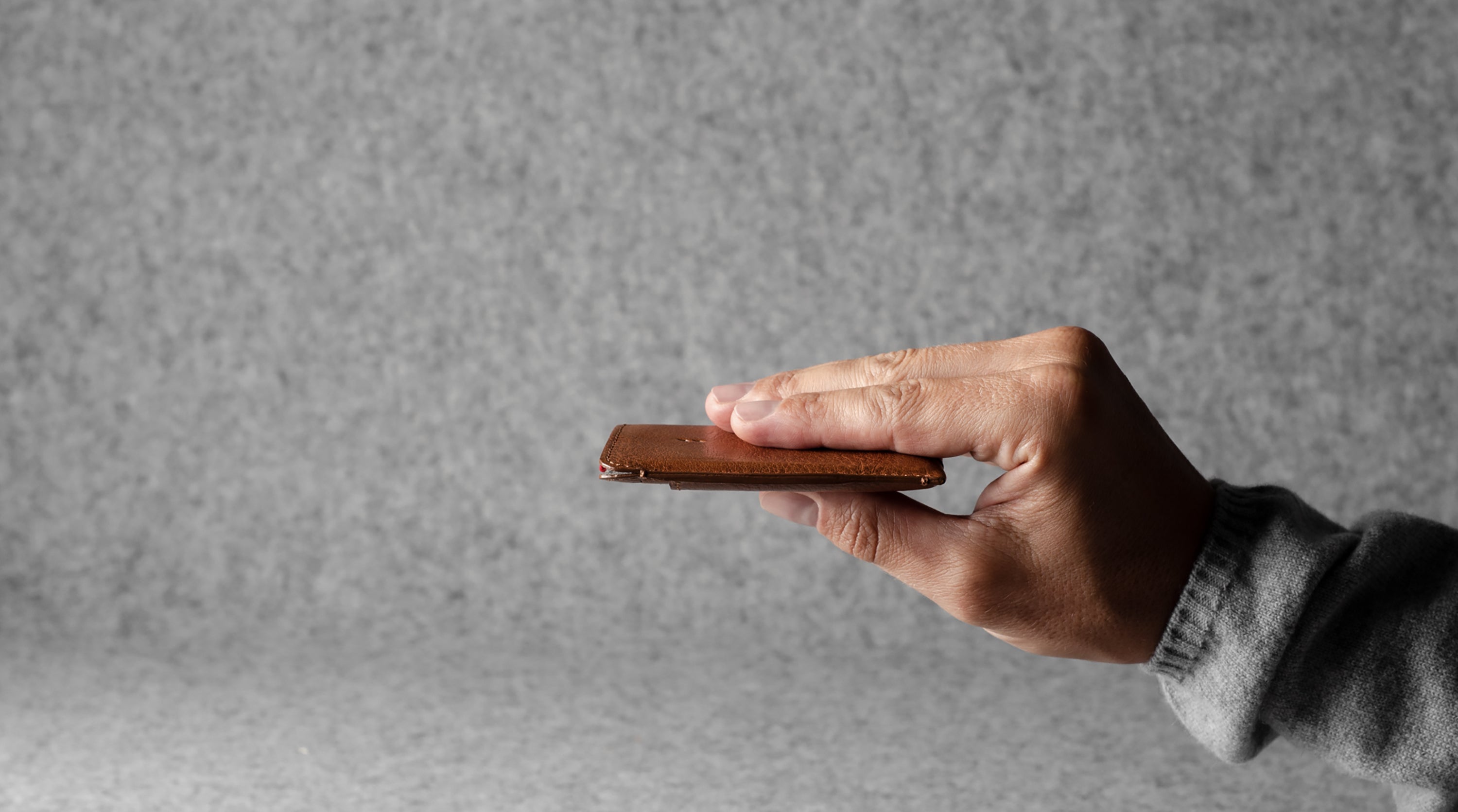 Hand holding a brown leather wallet against a gray background