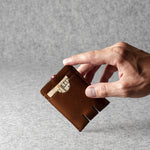 Hand holding a brown leather wallet with a gold buckle on a gray background