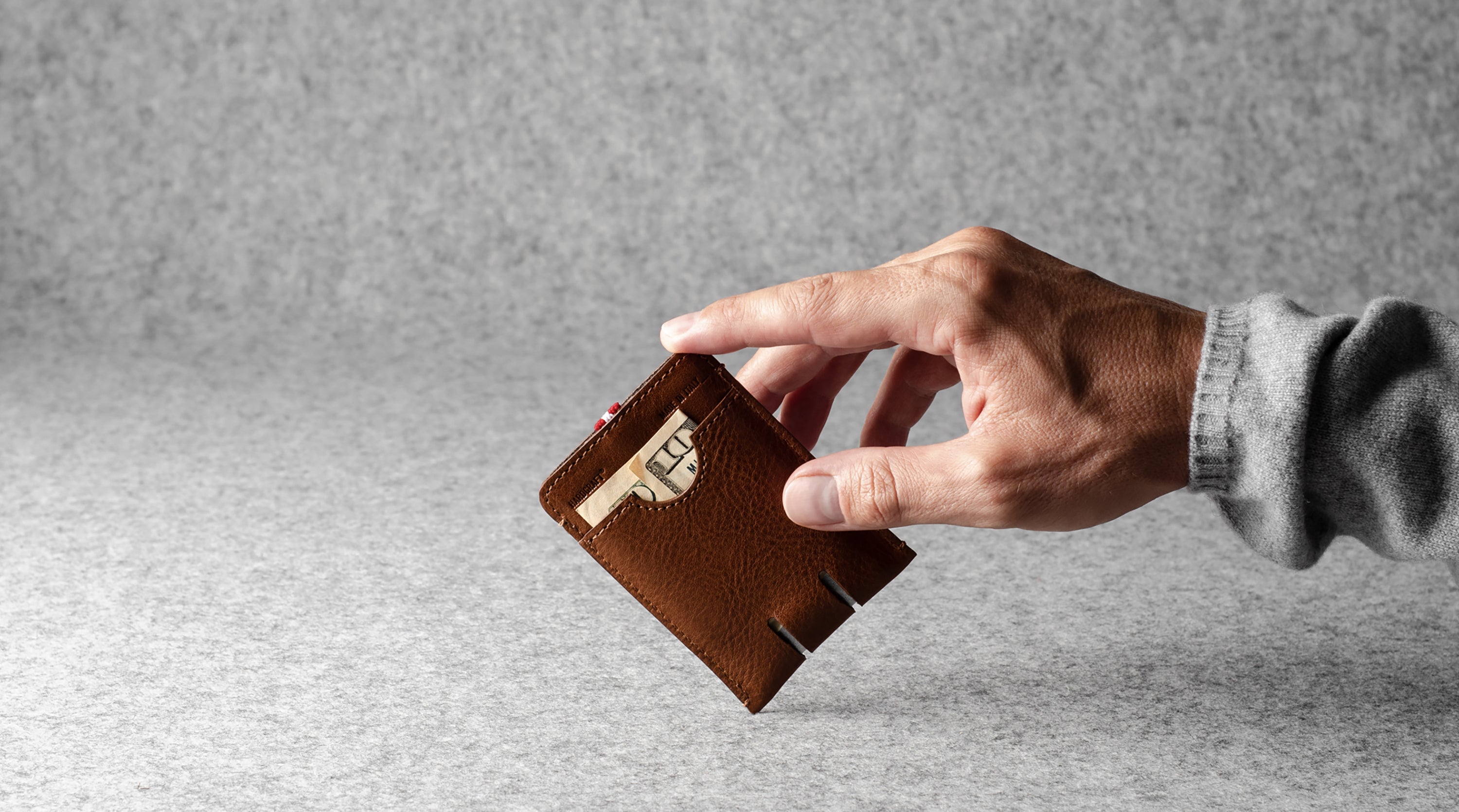 Hand holding a brown leather wallet with a gold buckle on a gray background