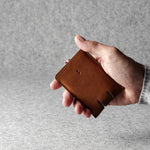 Hand holding a brown leather wallet against a gray background