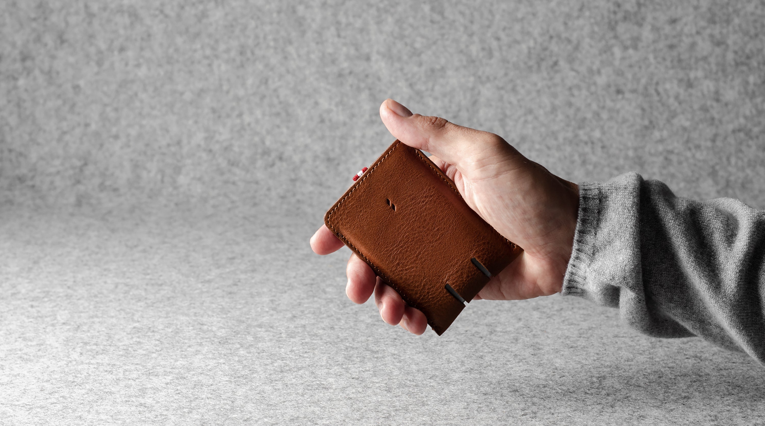 Hand holding a brown leather wallet against a gray background