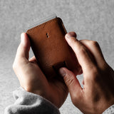 Person holding a brown leather wallet against a gray background