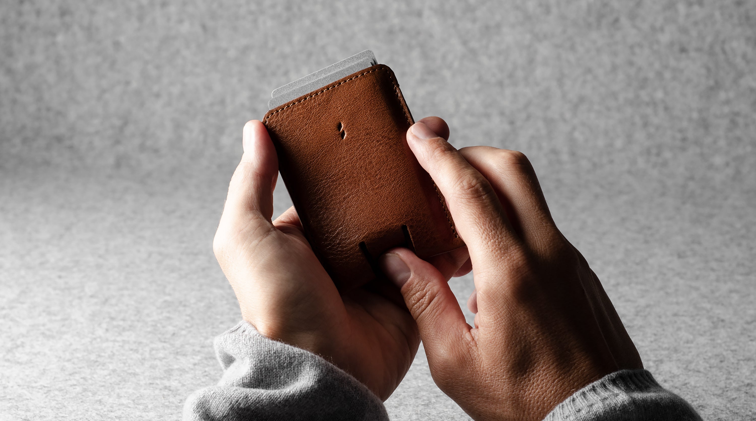 Person holding a brown leather wallet against a gray background