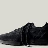 A single black suede sneaker with laces, set against a white background.