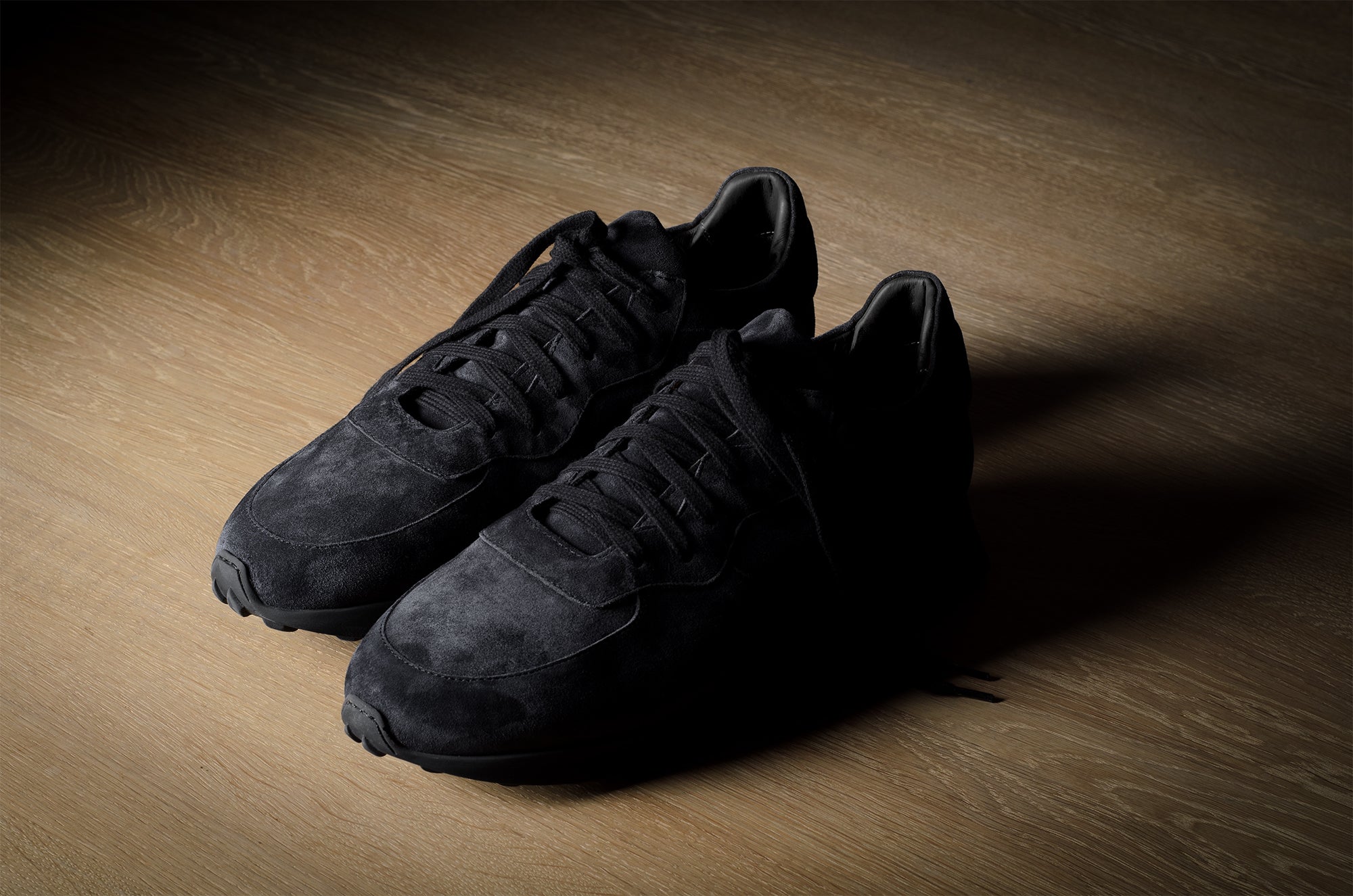 Black suede sneakers on a grey and brown wood background.