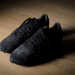 Black suede sneakers on a grey and brown wood background.