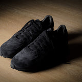 Black suede sneakers on a grey and brown wood background.