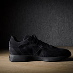 Black suede sneakers on a grey and brown wood background.