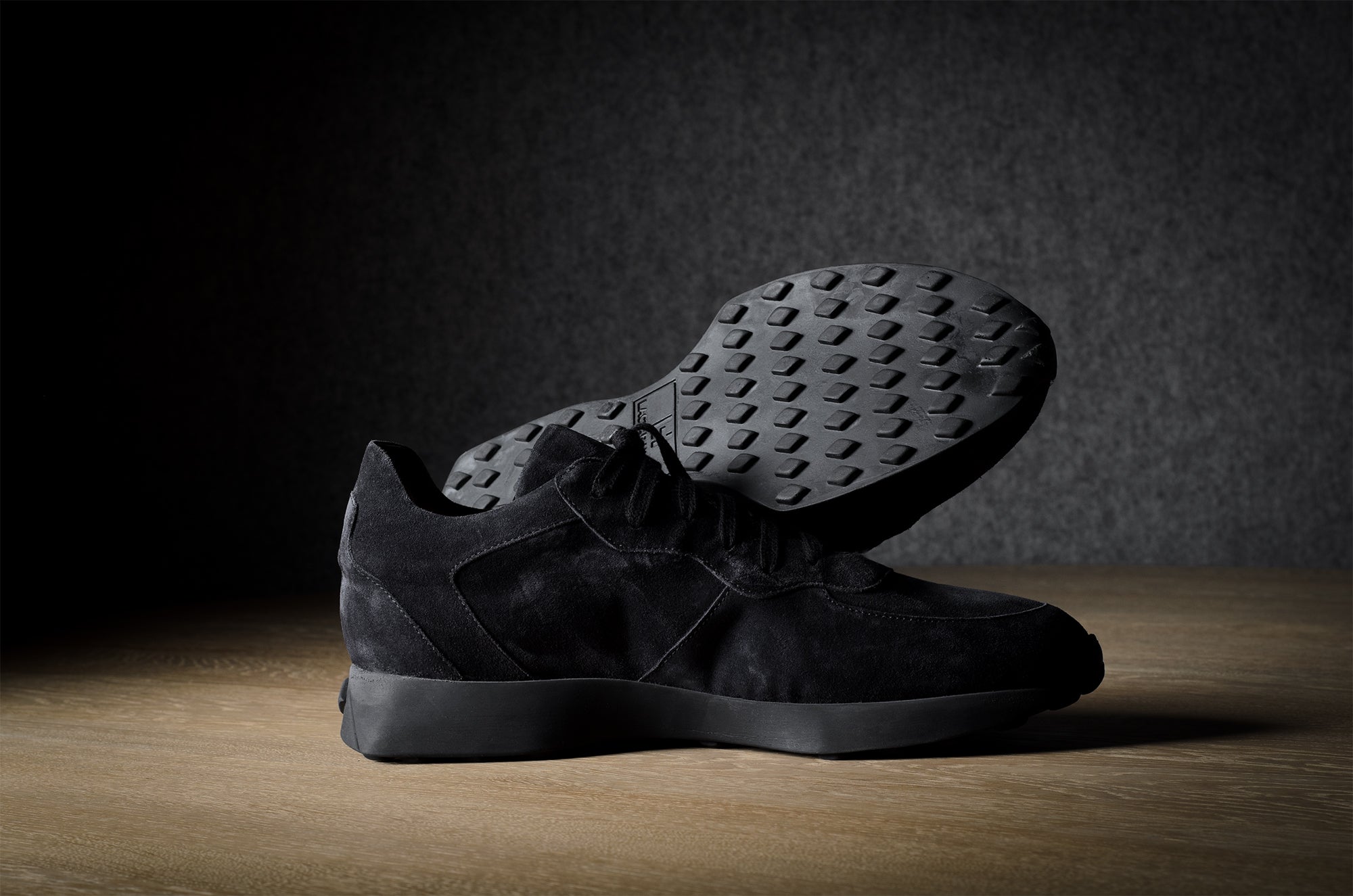 Black suede sneakers on a grey and brown wood background.
