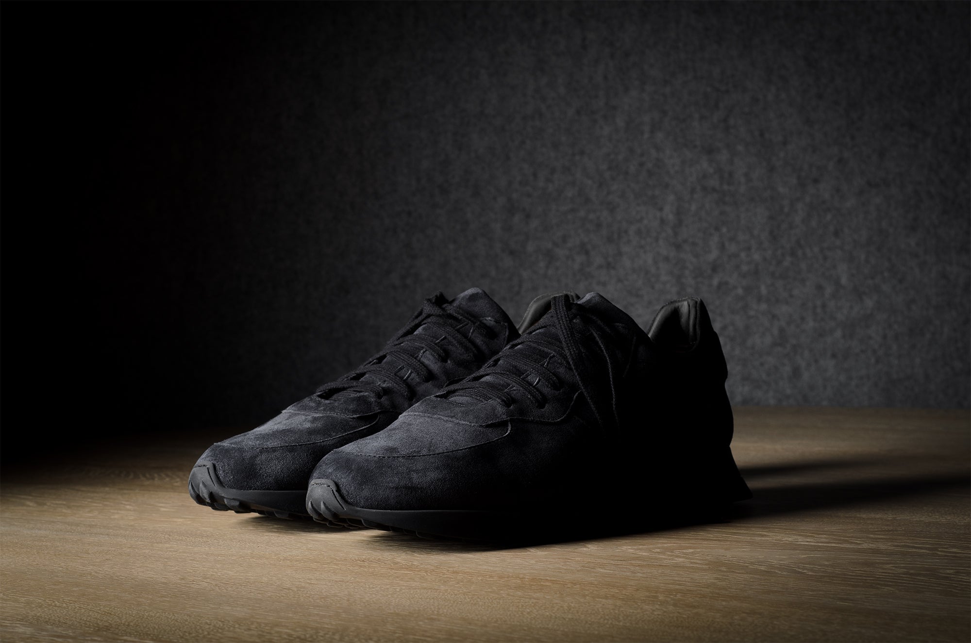 Black suede sneakers on a grey and brown wood background.