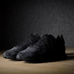 Black suede sneakers on a grey and brown wood background.