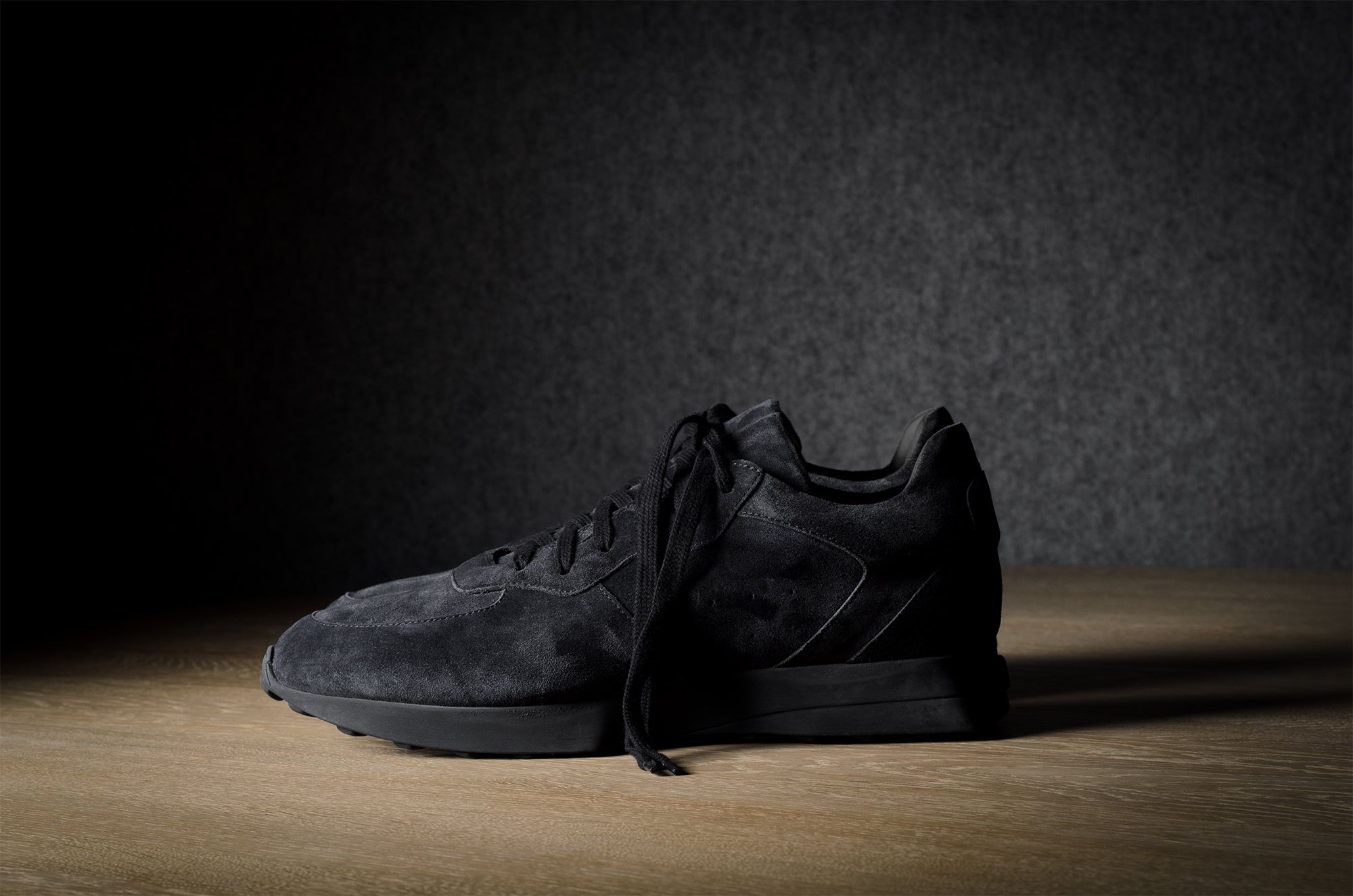 Black suede sneakers on a grey and brown wood background.