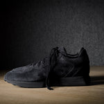 Black suede sneakers on a grey and brown wood background.