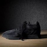 Black suede sneakers on a grey and brown wood background.