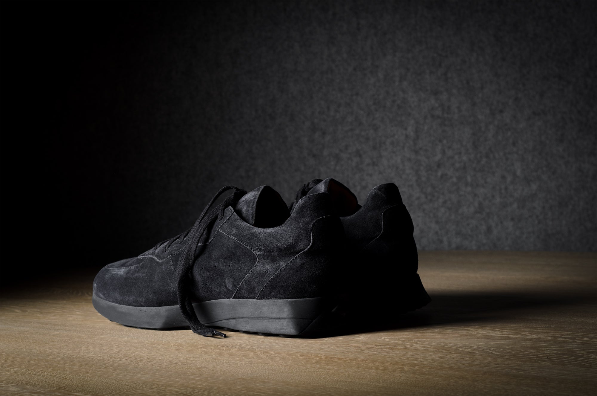 Black suede sneakers on a grey and brown wood background.