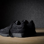 Black suede sneakers on a grey and brown wood background.