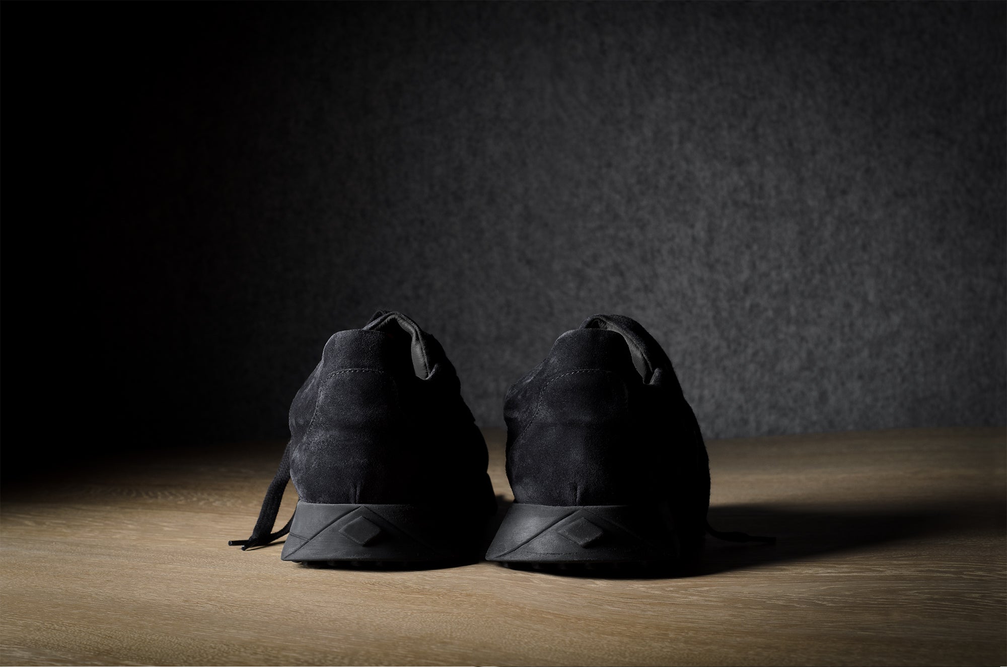 Black suede sneakers on a grey and brown wood background.