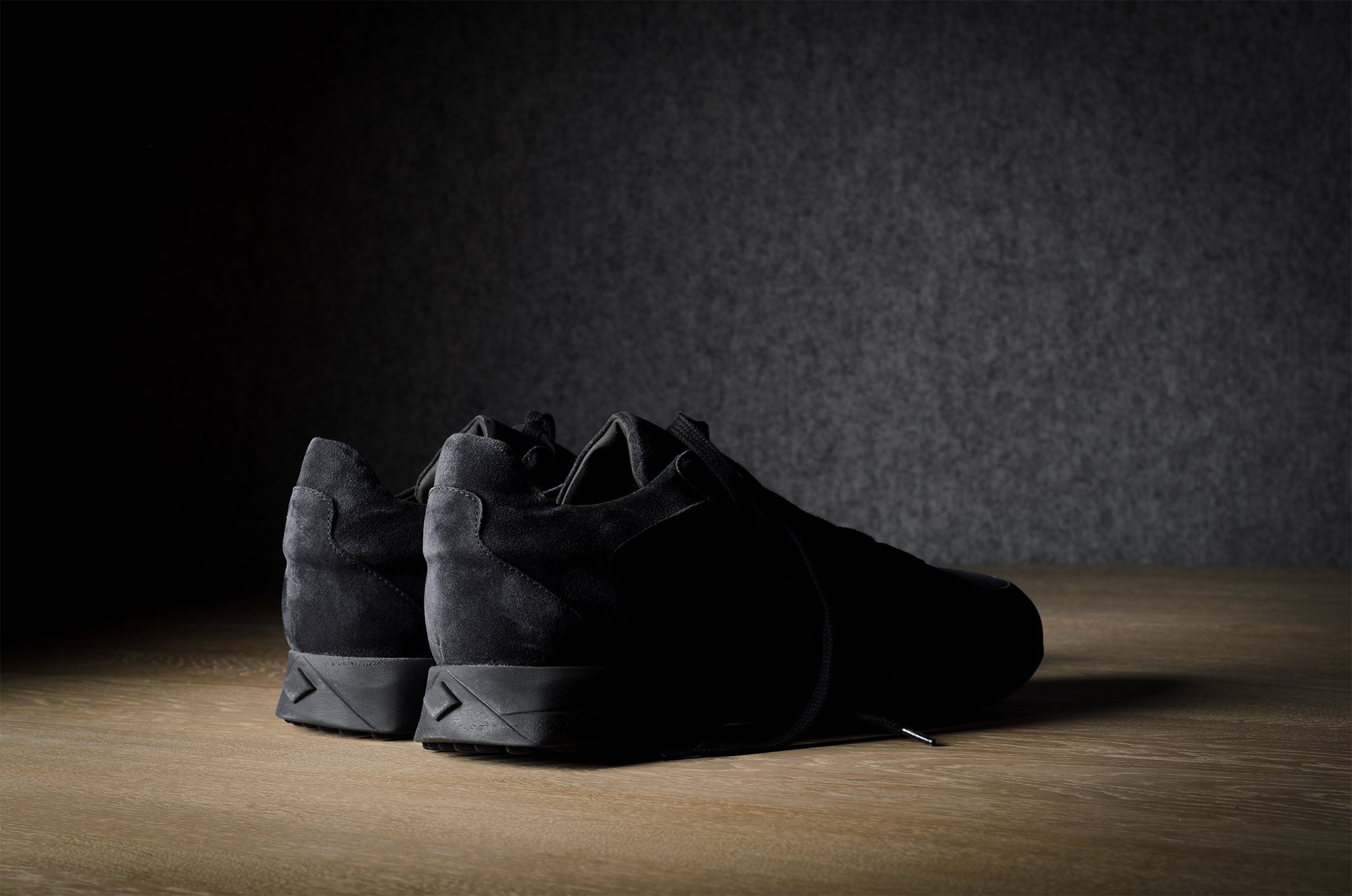 Black suede sneakers on a grey and brown wood background.