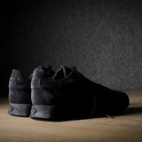 Black suede sneakers on a grey and brown wood background.