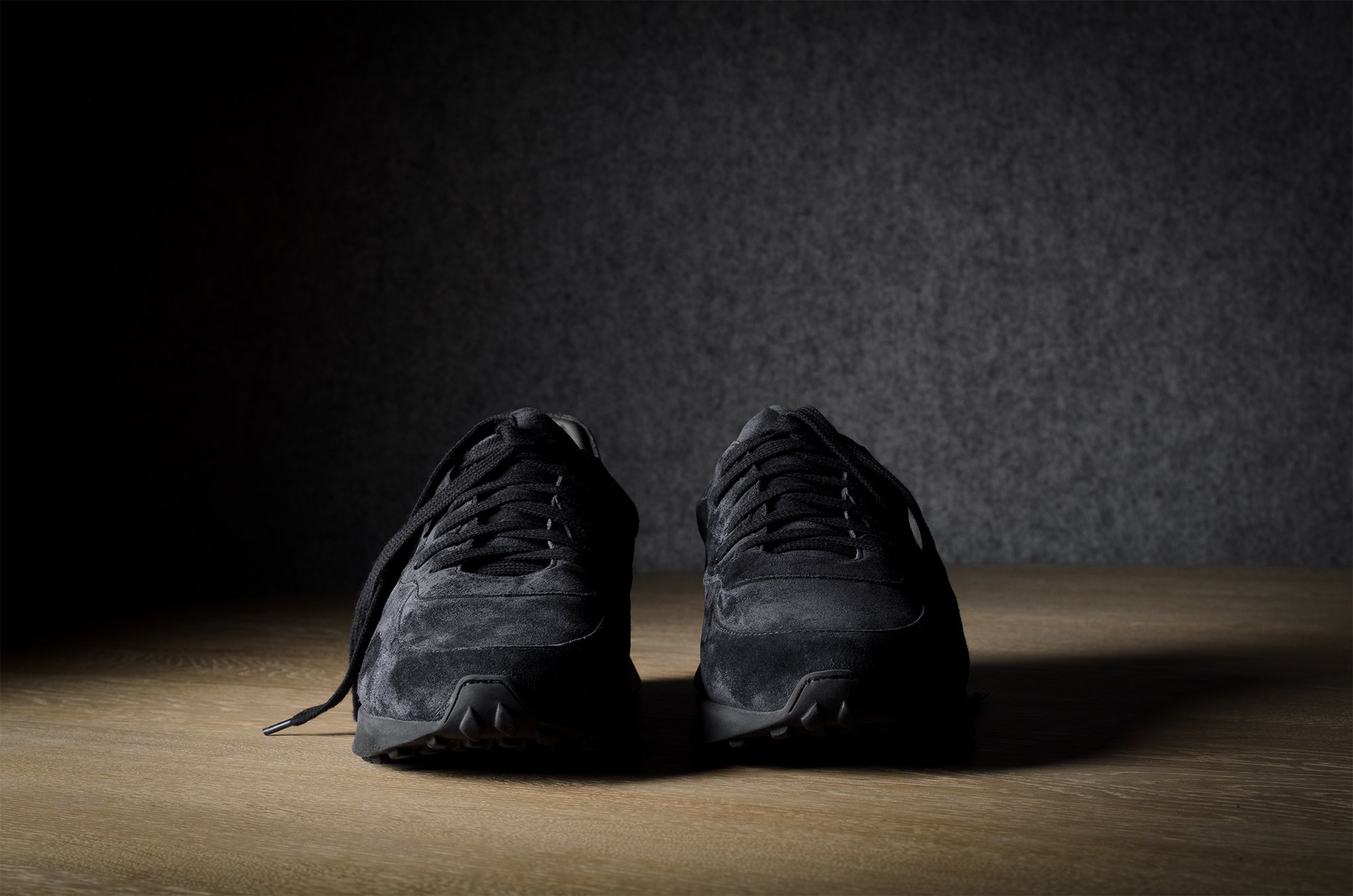 Black suede sneakers on a grey and brown wood background.