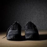 Black suede sneakers on a grey and brown wood background.