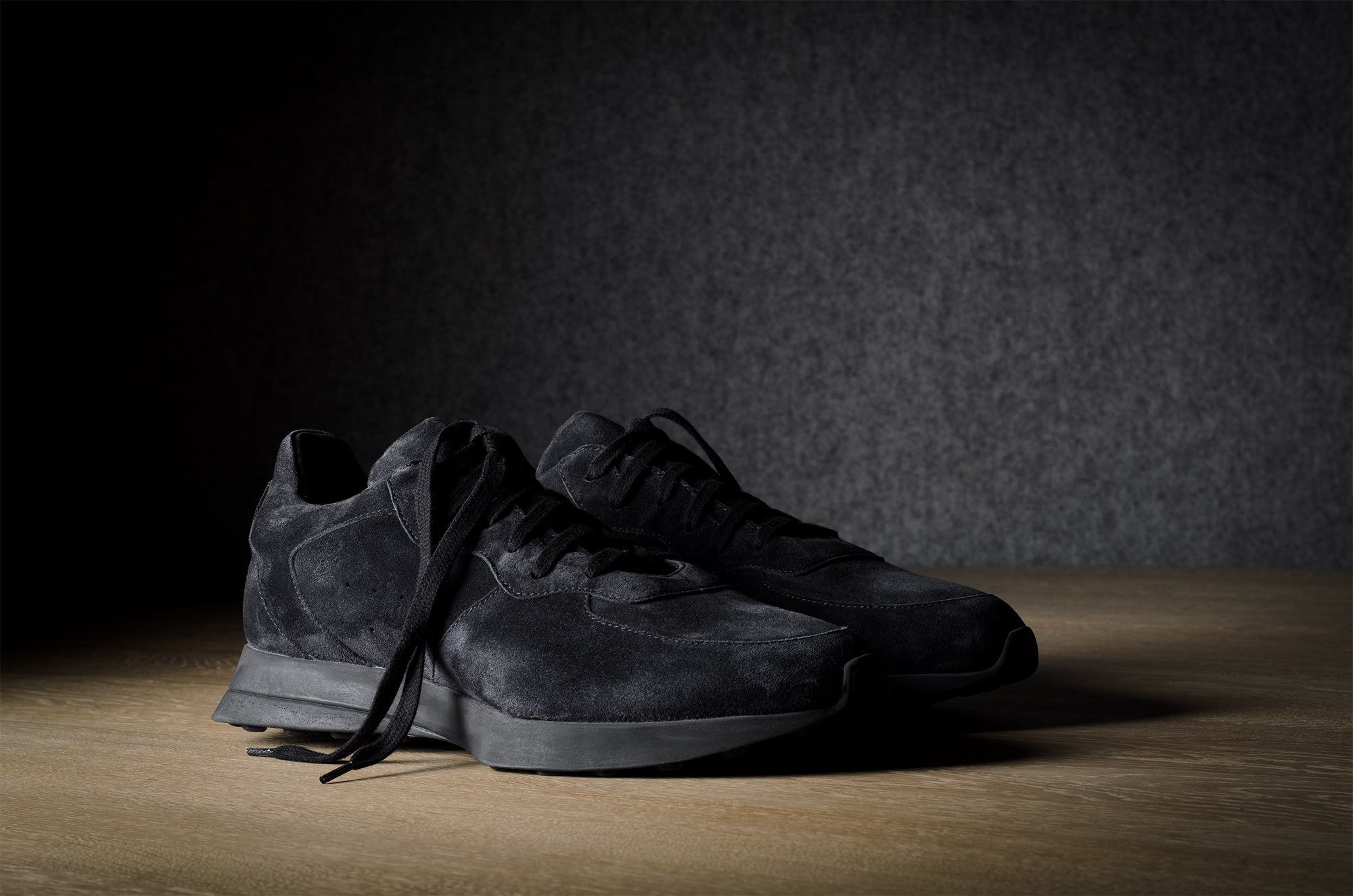 Black suede sneakers on a grey and brown wood background.