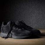 Black suede sneakers on a grey and brown wood background.