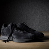 Black suede sneakers on a grey and brown wood background.